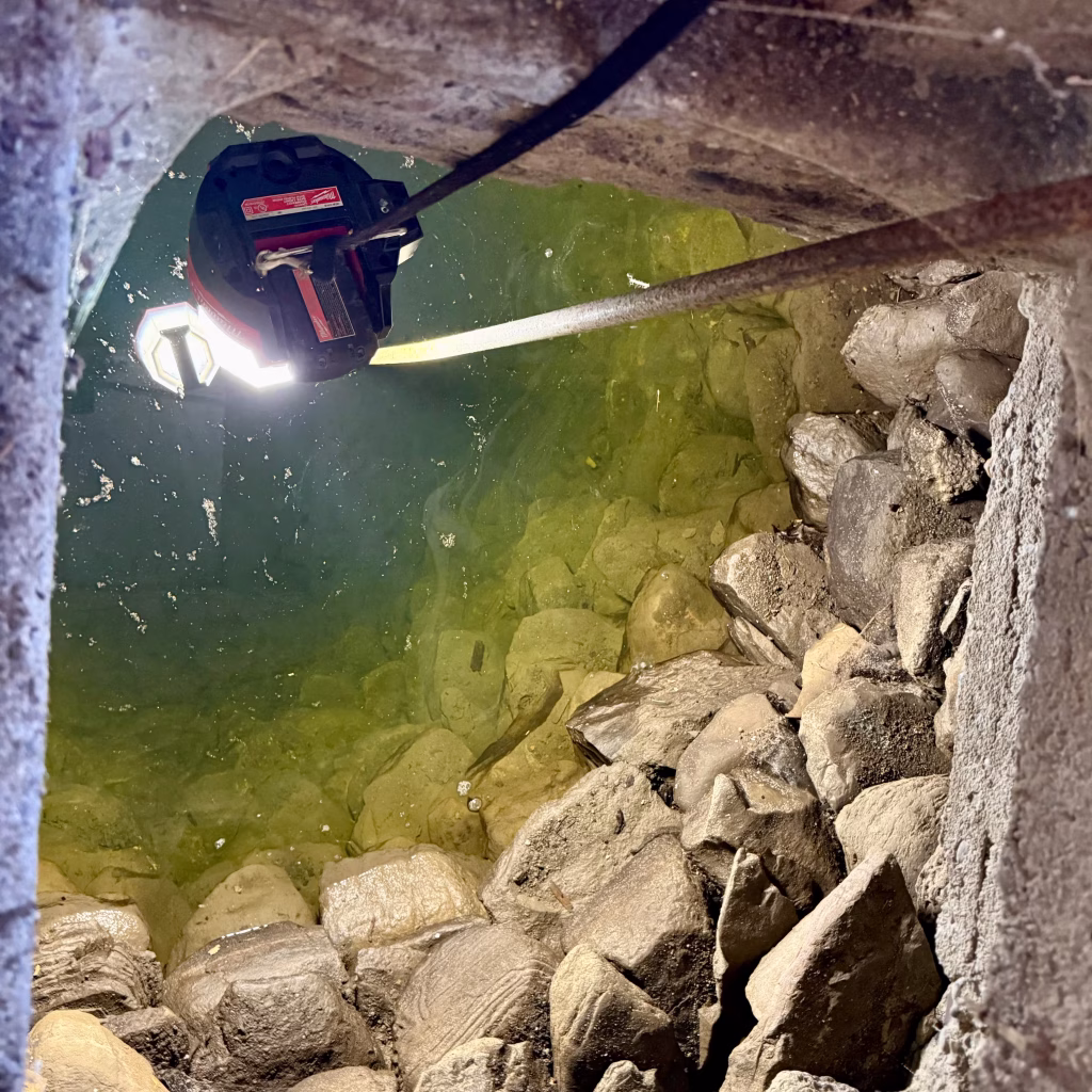 Close-up of the stone-lined walls and clear water inside a historic hand-dug well uncovered beneath the barn during renovation at Wiggly Goat Farm.
